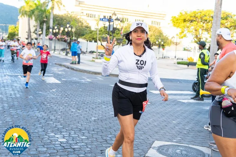 Una atleta con un número de identificación en su cintura saluda a la cámara mientras corre en una carrera en la República Dominicana.
