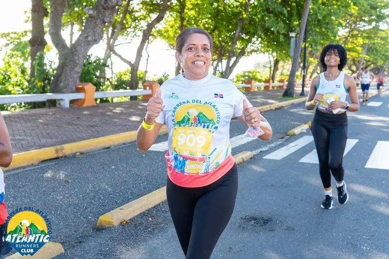 Una atleta con un número de participación en el pecho corre con alegría en una carrera al aire libre.