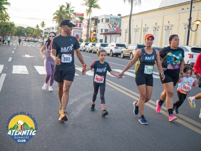 Un grupo de corredores participa en una carrera en la calle, con palmeras y edificios en el fondo.