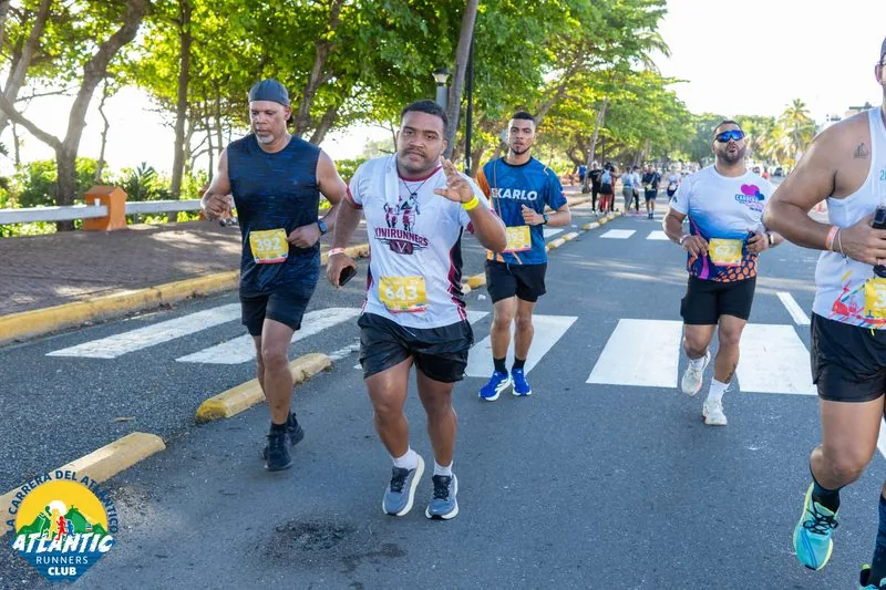 Imágen de corredores en una carrera con bibs visibles y un entorno urbano al fondo.