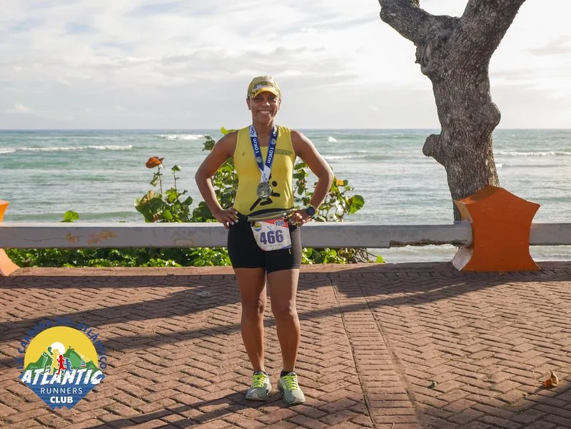 Una atleta con medalla y bib posa en un entorno costero con el mar en el fondo