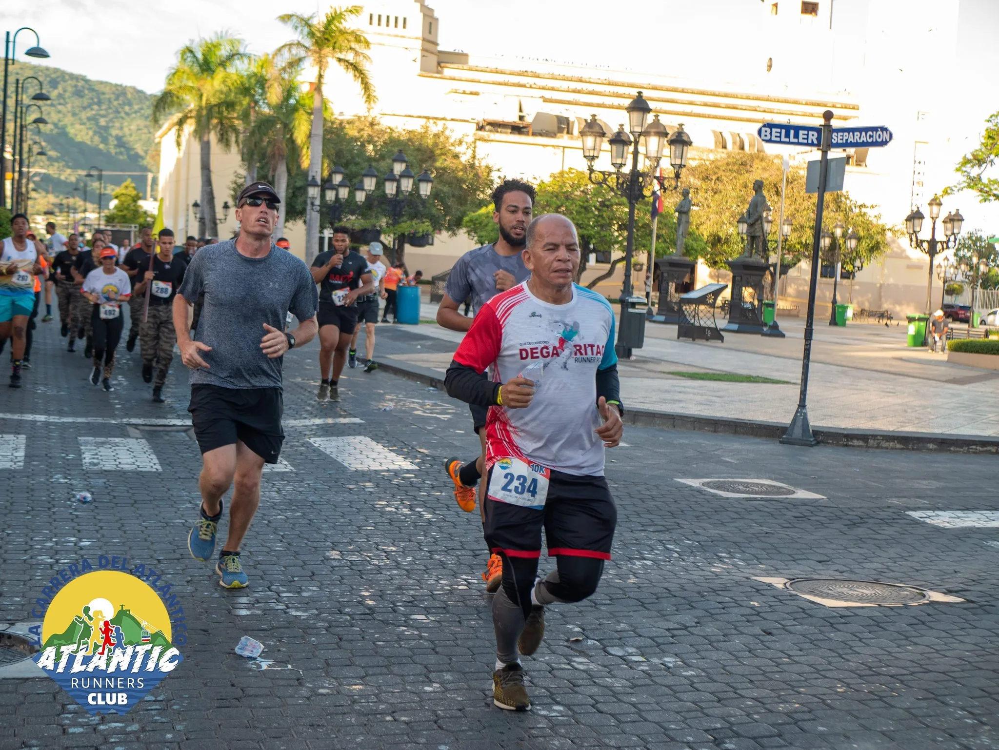 Imagen de corredores en una carrera atlética con edificios y monumentos en el fondo.