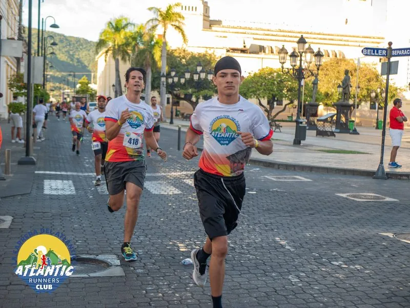 Imágen de corredores en una carrera urbana con edificios y palmeras en el fondo.